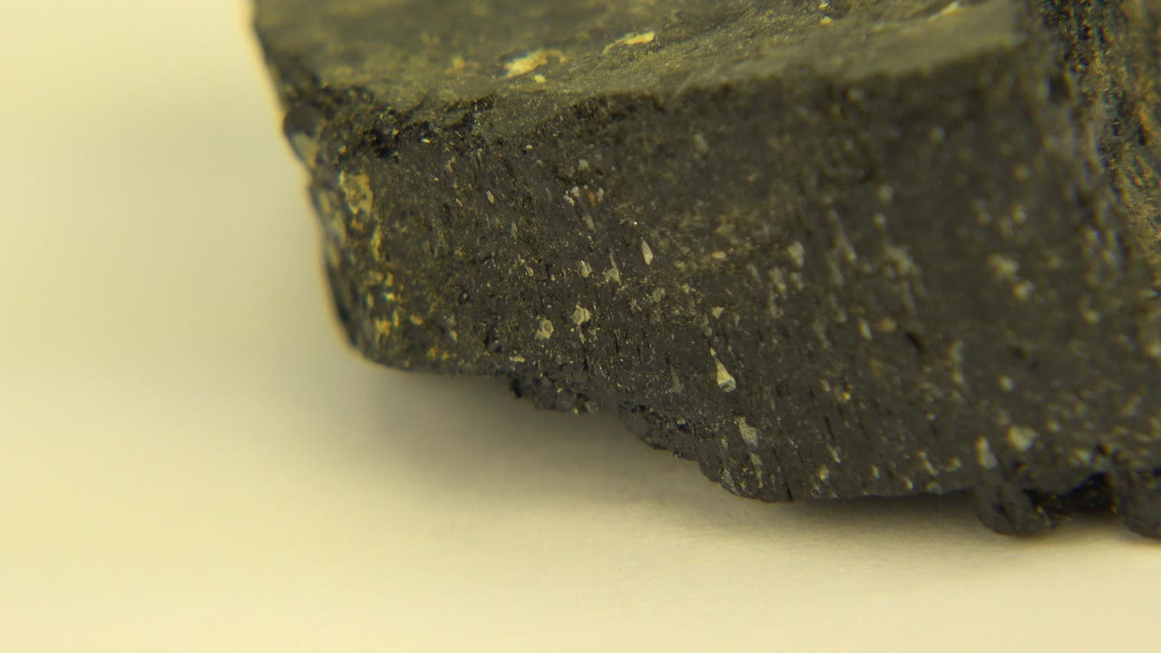 A tight close-up in Westminster, Colorado shows the lower edge of a dark rock with small yellow flecks on a white surface, with no visible people.