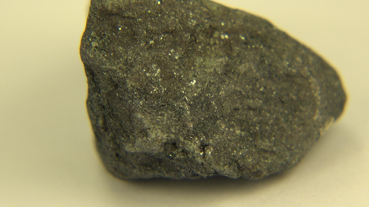 Close view of a dark glittering rock on a pale surface in Westminster, Colorado, with silver flecks visible and no visible people.