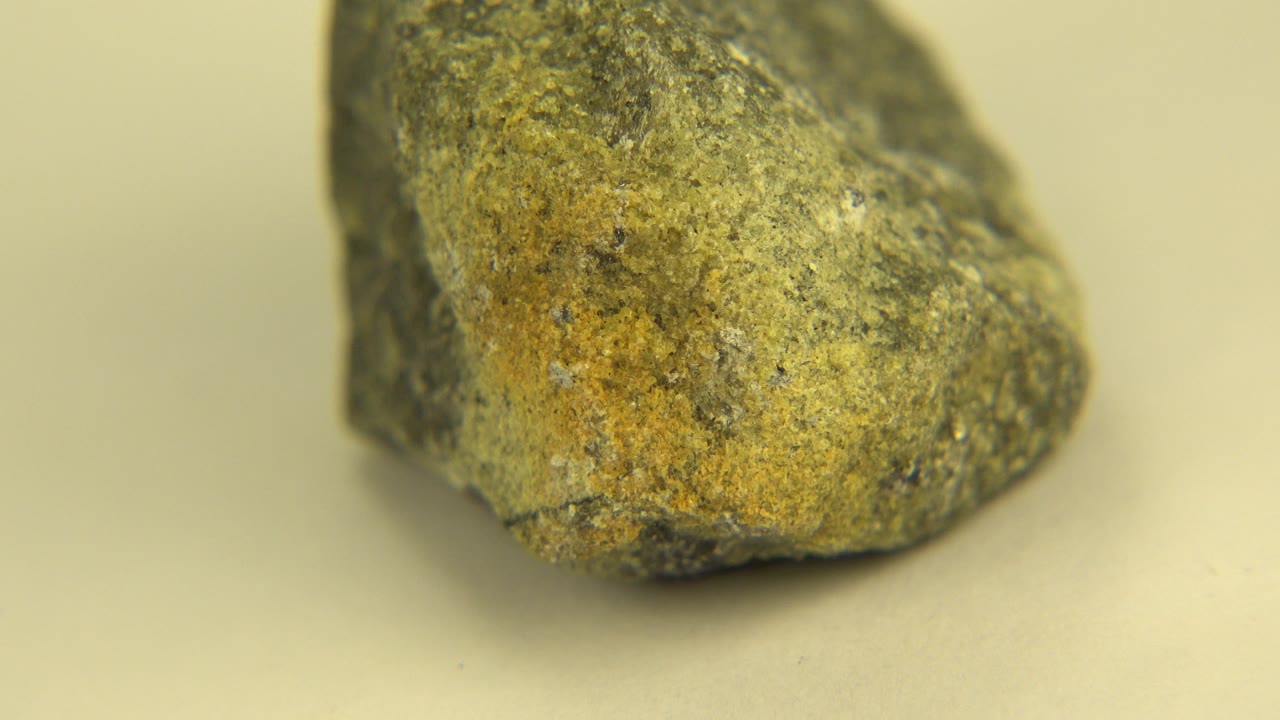 A rough gray-green sandstone piece sits close to camera on a pale flat surface in Westminster, Colorado, with no visible people.