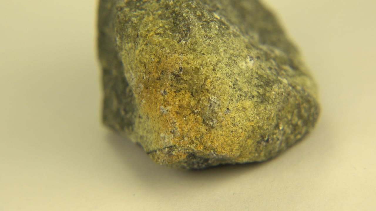 The sandstone remains large in frame on the pale surface in Westminster, Colorado, showing a rounded face with ocher mottling and no visible people.
