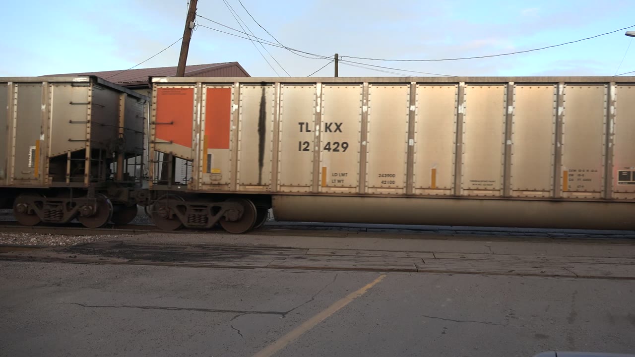 Two connected freight cars pass along tracks beside pavement.