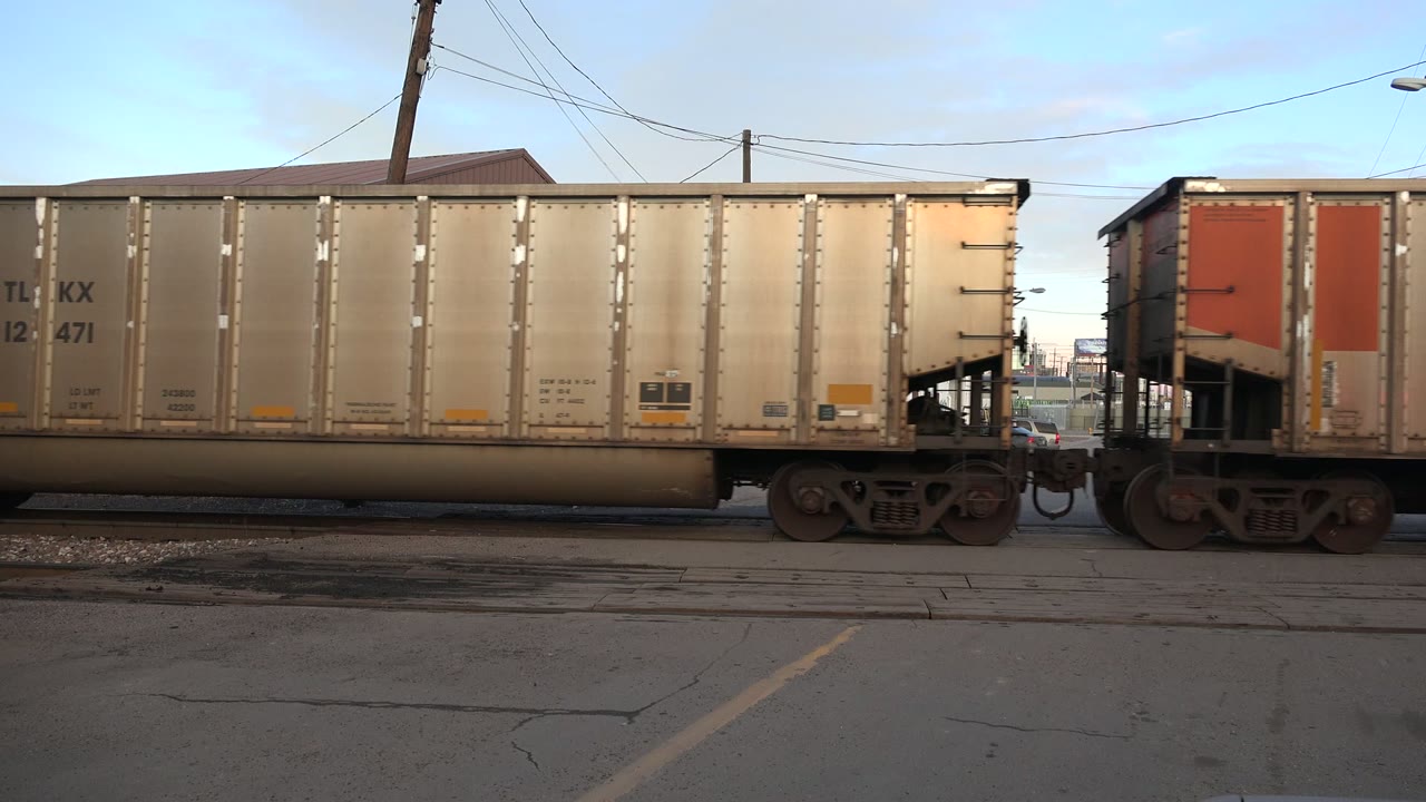 Two freight car sections move through the Westminster frame, with a red crossing signal visible near the right edge and no visible people.