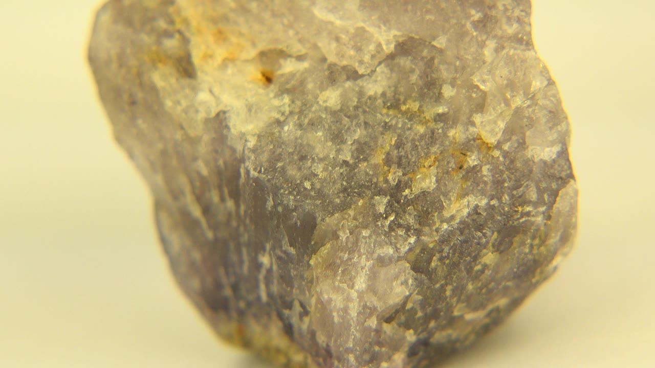 Close view of a rough gray-brown rock on a pale yellow floor in Westminster, Colorado, with white mineral flecks and no visible people.