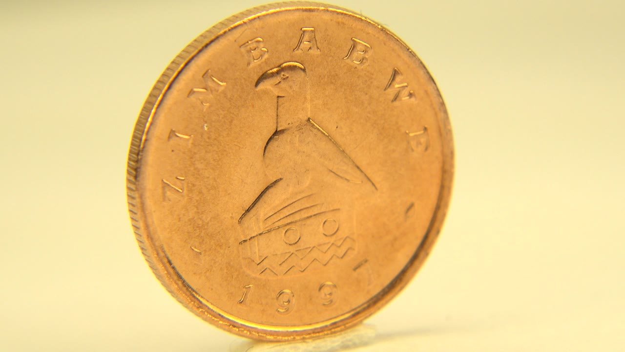 Gold-colored coin standing face-on on a pale yellow surface.