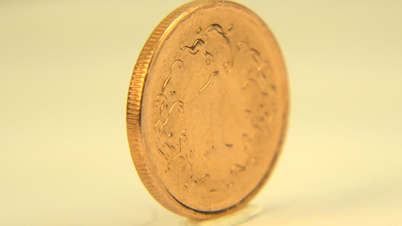 Gold coin turned partly toward camera on a pale surface.