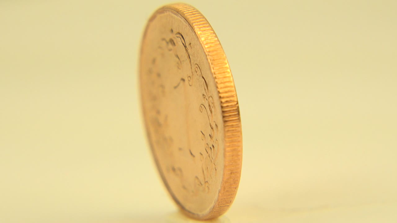 A copper-gold coin stands tilted on its edge in a warm close-up from Westminster, Colorado, with a soft yellow background and no visible people.