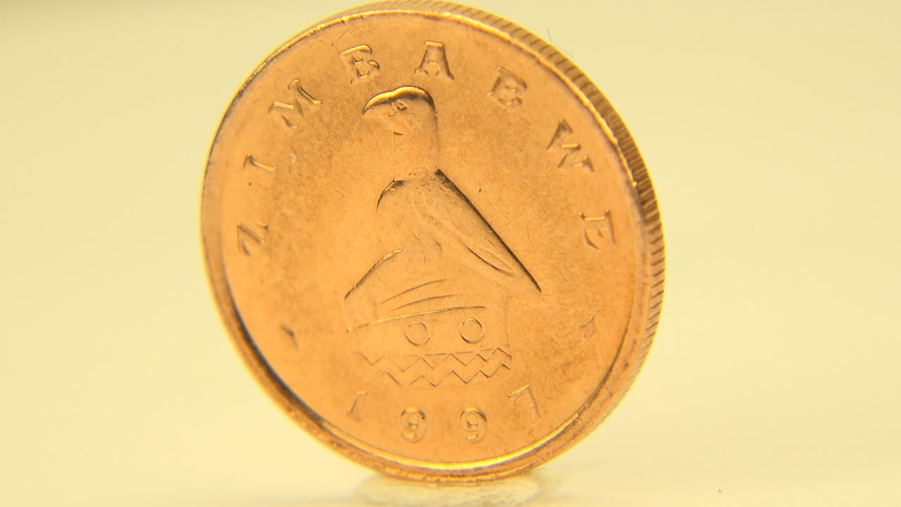 The coin remains nearly front-facing on the tabletop in the Westminster, Colorado clip, with warm yellow light and no visible people.
