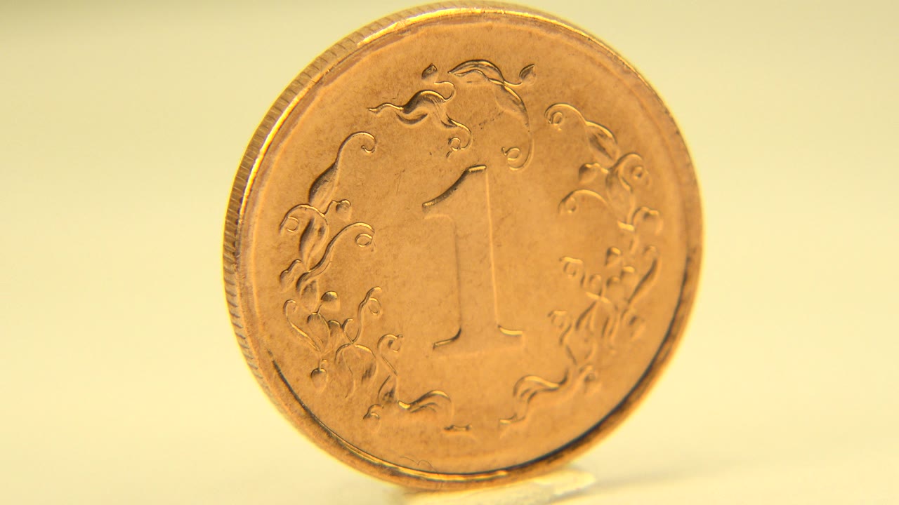 A bronze or golden penny stands nearly face-on on a pale surface in Westminster, Colorado, with warm yellow light and no visible people.