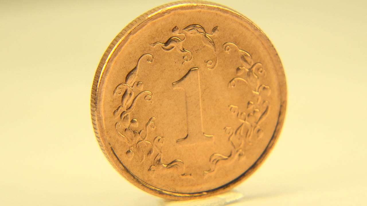 The penny remains mostly face-on in the close-up, its raised number and floral markings softened by shallow focus, with no visible people.