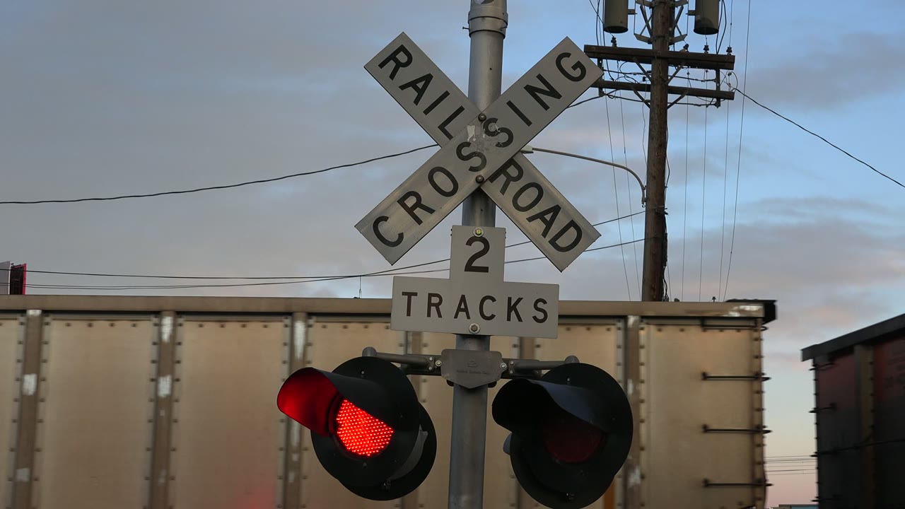 Railroad crossing sign and red warning light with freight cars behind it.