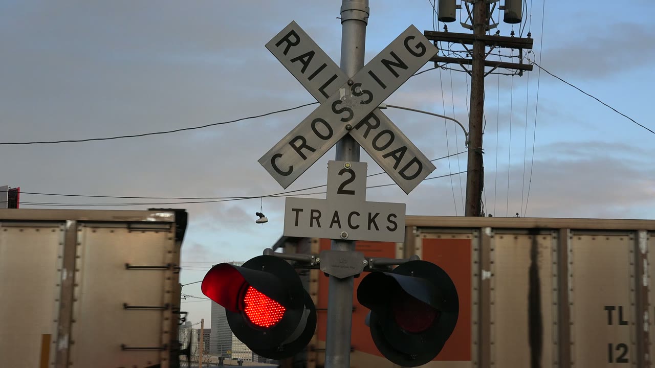 One second in, the Westminster railroad crossing remains centered while the red signal glows and a freight car with an orange panel moves behind the sign, with no visible people.