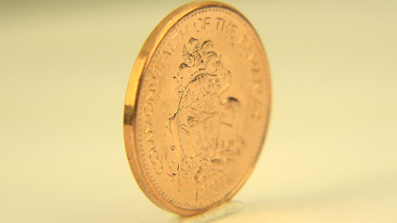 A gold-toned coin stands upright at a slight angle in Westminster, Colorado footage, with soft yellow light and no visible people.