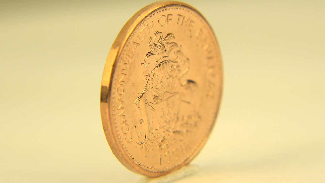 The upright coin remains angled in the frame, showing more of its face and engraved markings against a warm yellow backdrop, with no visible people.