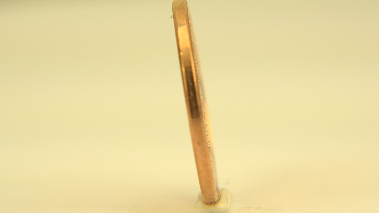At 0:00, the Bahamas one-cent coin is seen almost edge-on under warm white light in Westminster, Colorado, with no visible people.
