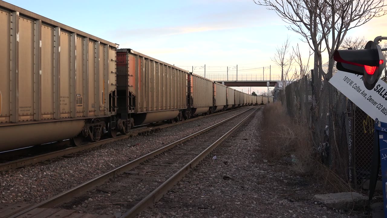 Freight train passing beside railroad tracks and a red signal light.