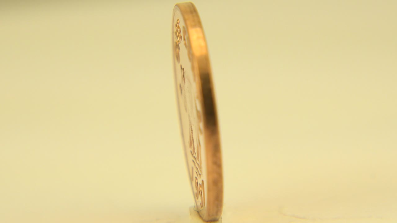 A British one-pound coin stands nearly edge-on on a pale surface in Westminster, Colorado, with warm yellow light and no visible people.