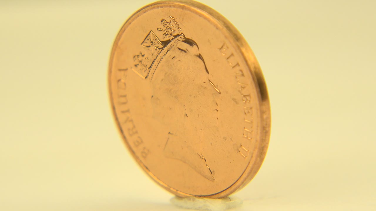 Close-up of a copper Bermuda penny in Westminster, Colorado, angled toward the Queen Elizabeth side under warm white light, with no visible people.
