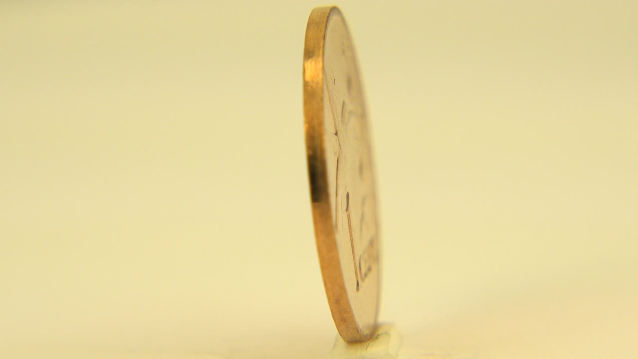 The copper Canadian penny remains mostly edge-on, slightly angled in the warm Westminster, Colorado home-video setup with no visible people.