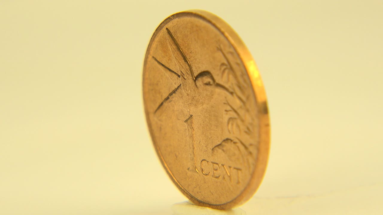 A yellow-gold coin stands on edge on a pale wooden table in Westminster, Colorado footage, with the one-cent face partly visible and no visible people.