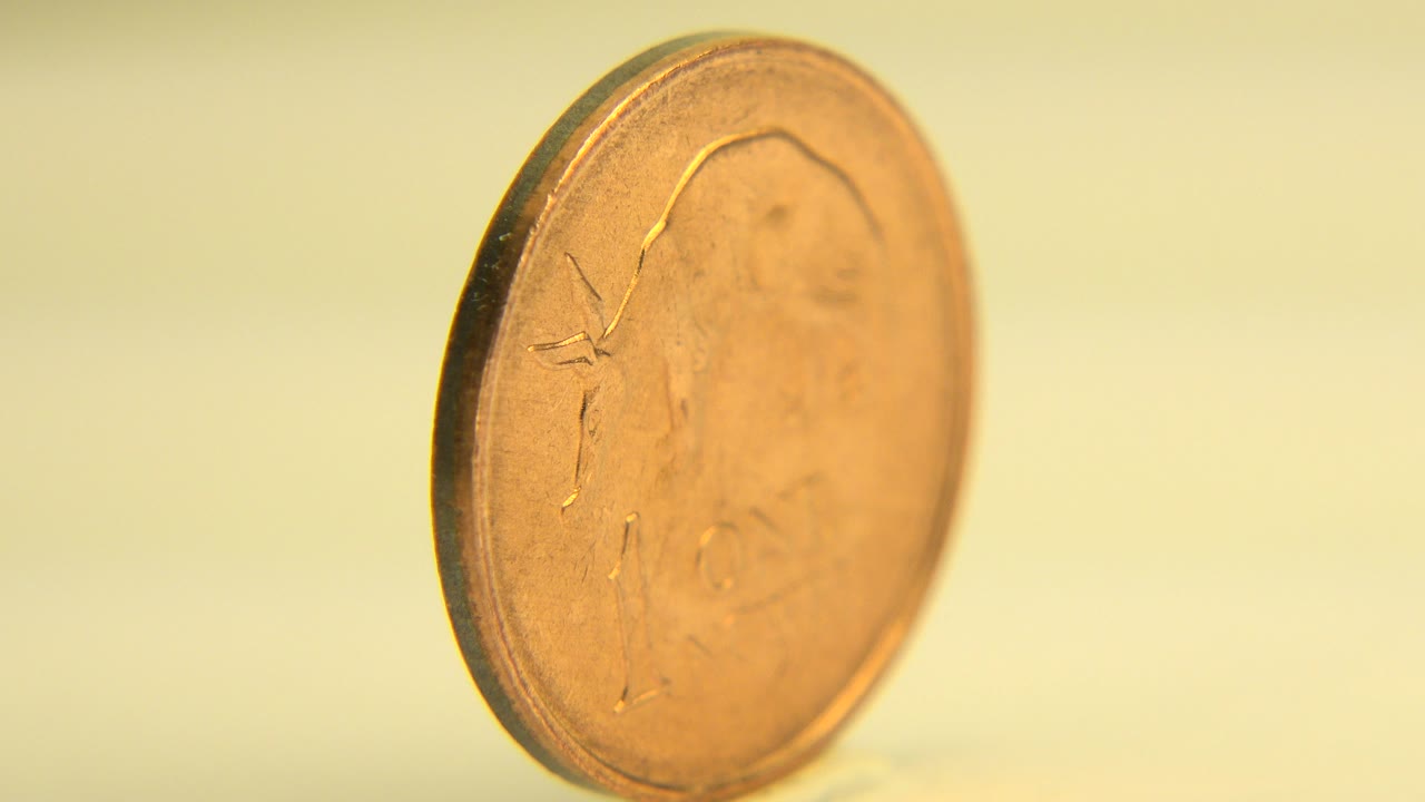 A copper one-cent coin stands at a slight angle on a pale tabletop in Westminster, Colorado 2015 footage, with a warm yellow background and no visible people.