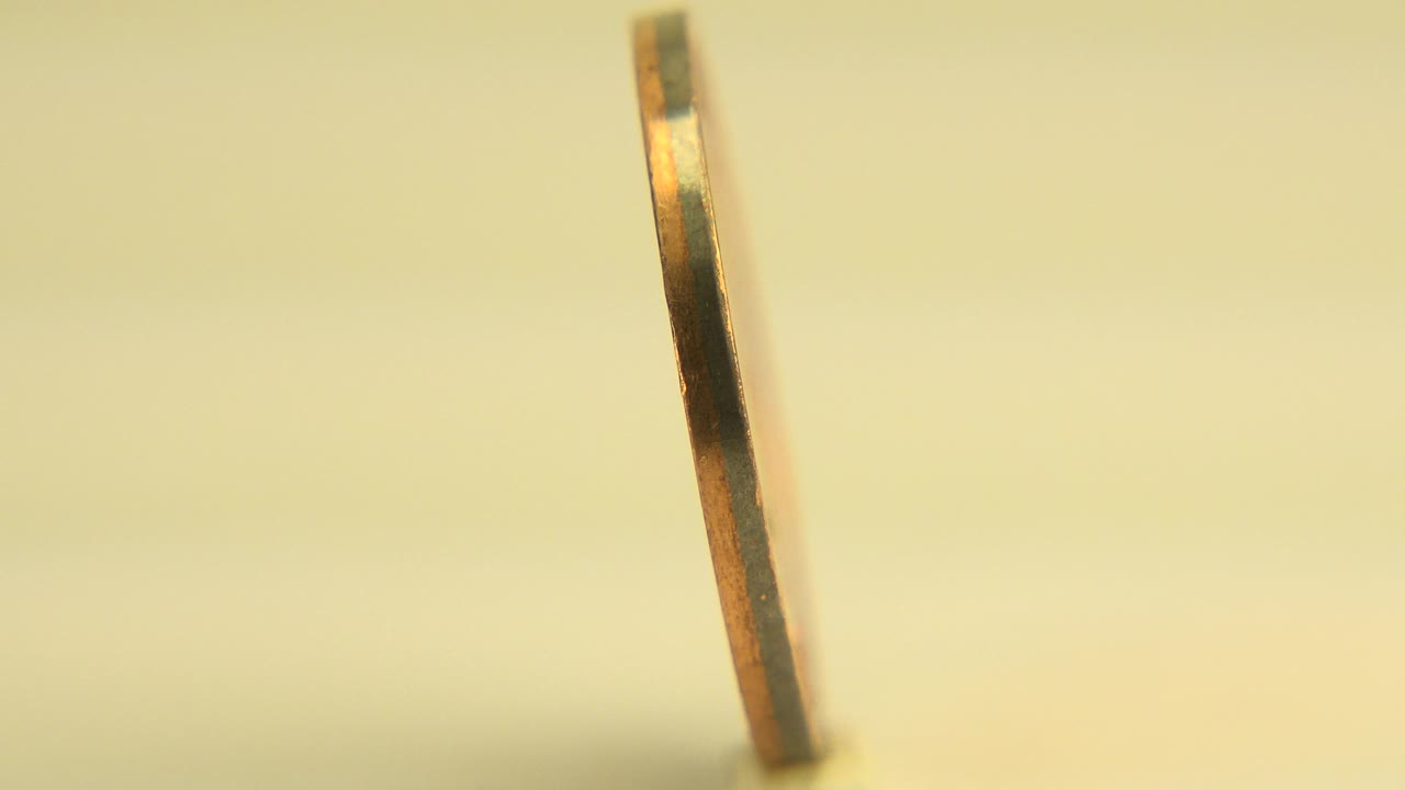 A thin upright gold-toned coin edge is seen in shallow focus in Westminster, Colorado, with a pale background and no visible people.