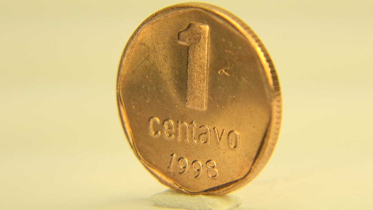 At 0:00, a gold-toned Argentinian 1 centavo coin stands upright on a pale surface in Westminster, Colorado, with the numbered face readable and no visible people.