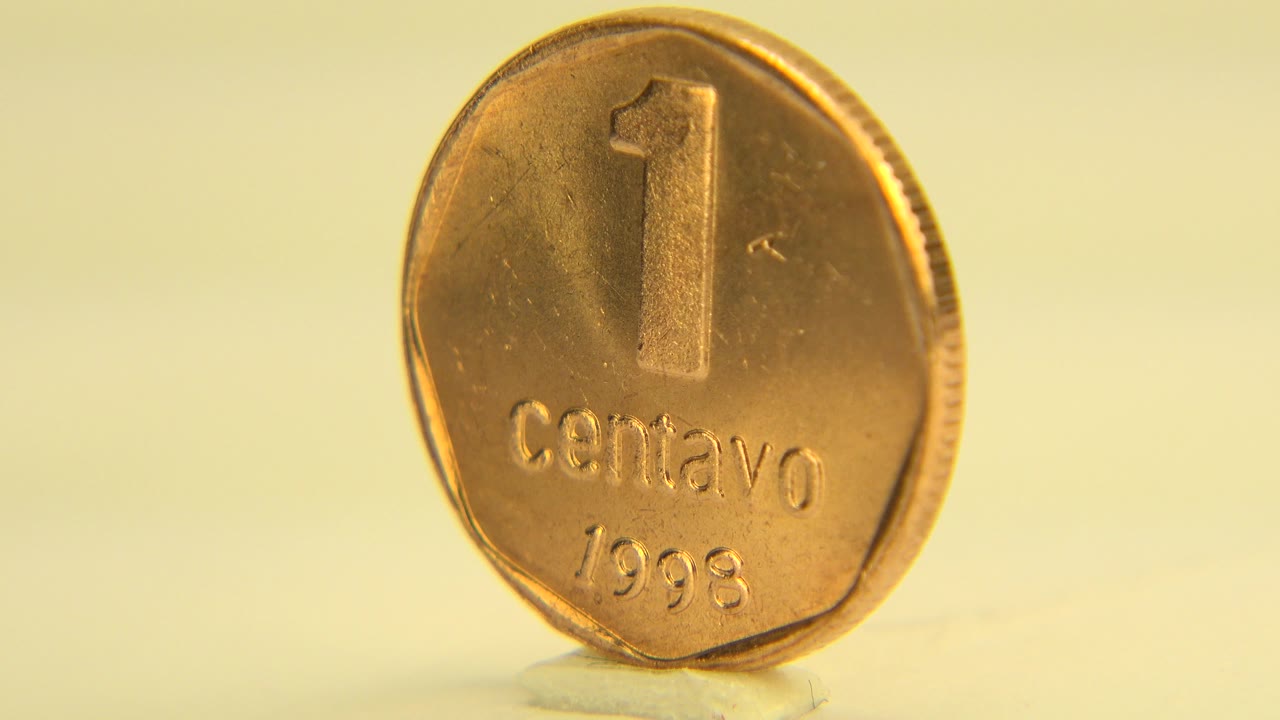 At 0:01, the upright centavo remains near front-facing on the pale surface in Westminster, Colorado, with warm light catching its raised lettering and no visible people.