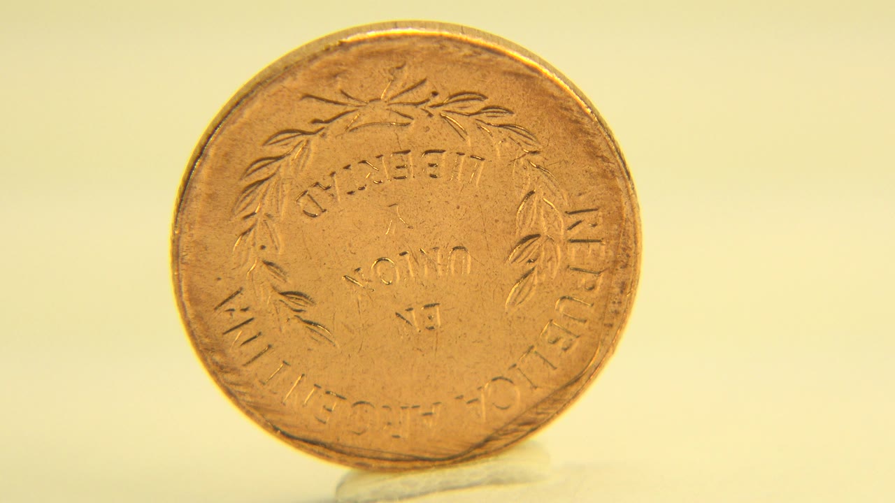 Front-facing worn golden penny stands upright on a pale yellow surface in Westminster, Colorado 2015 footage, with no visible people.
