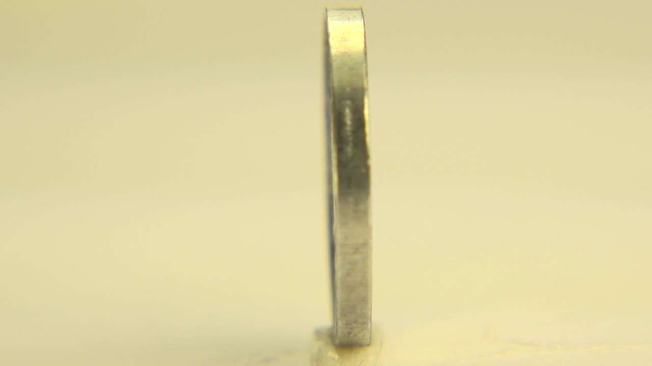 At the start of the Westminster, Colorado clip, the coin is nearly edge-on and upright on a pale yellow surface with warm light and no visible people.