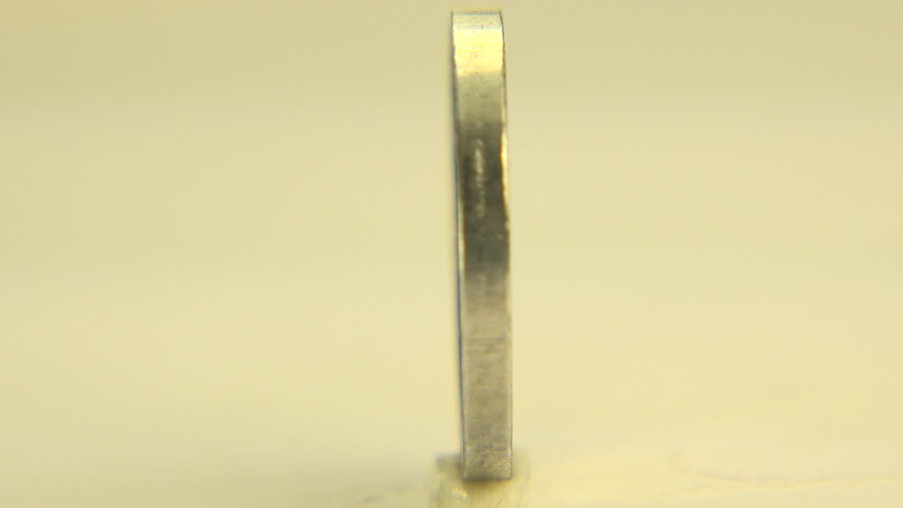 One second in, the Westminster, Colorado coin remains mostly edge-on, centered in warm light above a faint reflection, with no visible people.