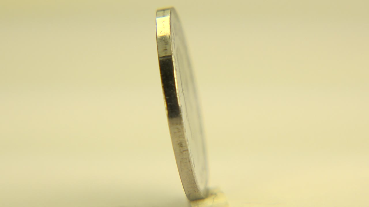 A narrow side view of a silver-toned El Salvador coin standing upright on a pale surface in Westminster, Colorado, with warm yellow background light and no visible people.