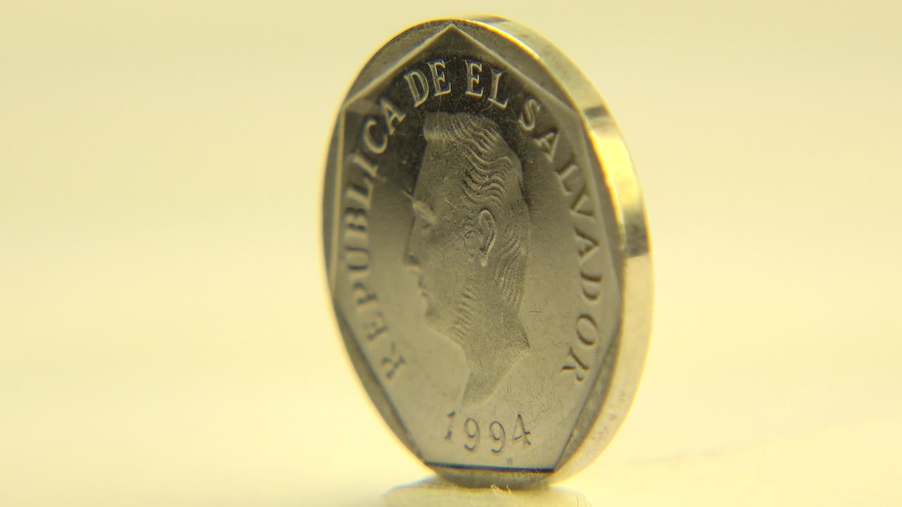 The coin remains upright near the center of the close-up frame, with the portrait side readable and no visible people.