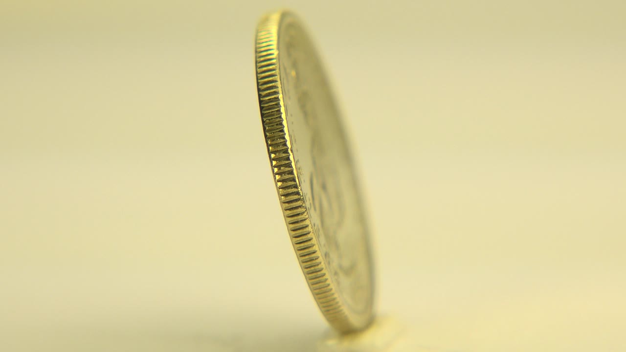 Gold coin standing edge-on against a pale yellow background.
