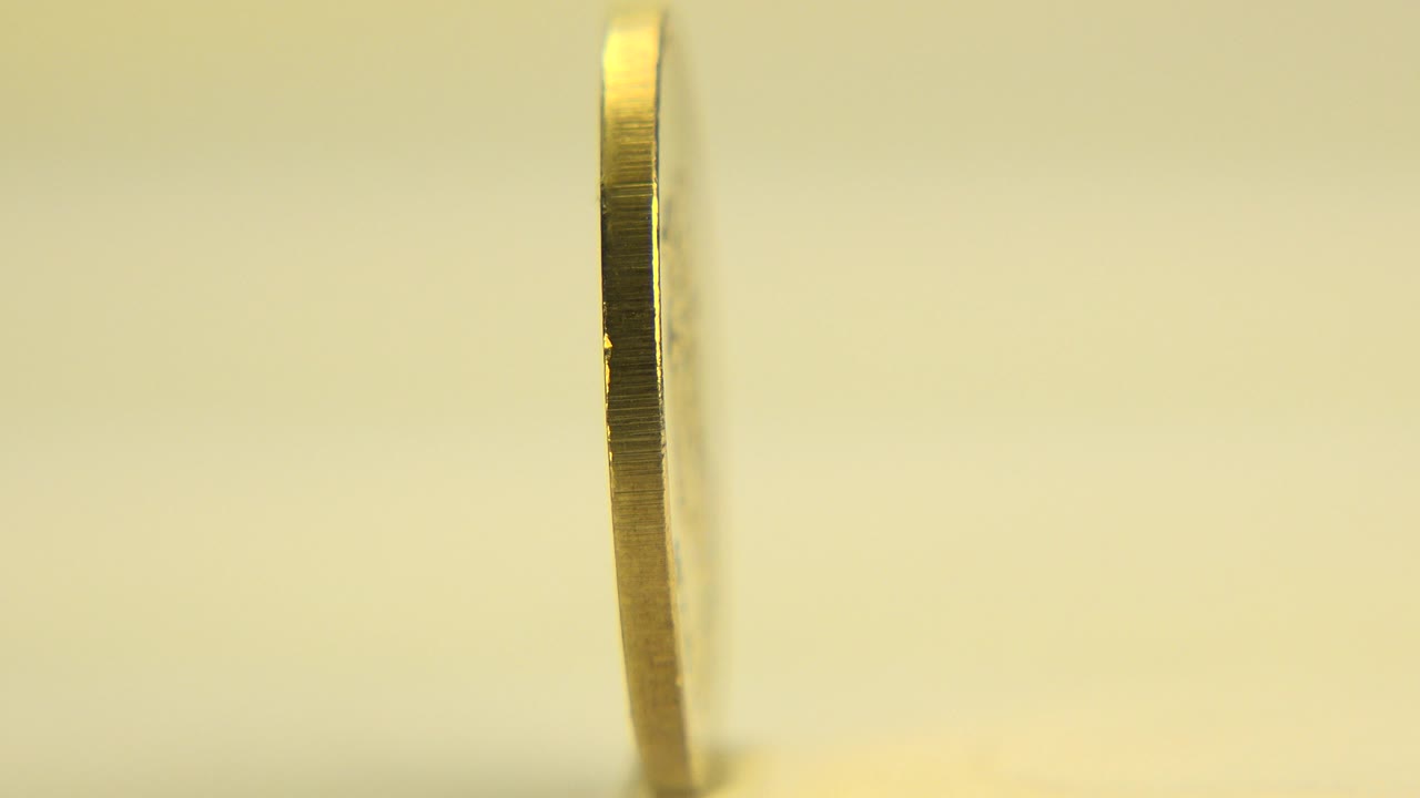 Thin edge of a gold coin upright on a pale surface.