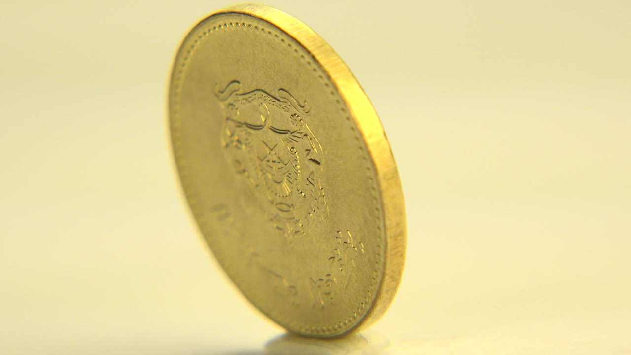 A gold-colored five centavo coin stands tilted on its edge on a pale surface in Westminster, Colorado, with warm light and no visible people.