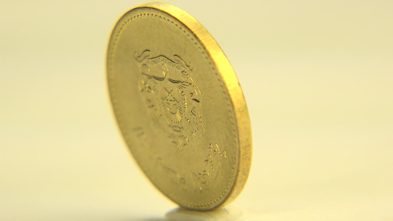 The coin remains upright and slightly angled as embossed details blur in warm light, with a plain pale background and no visible people.