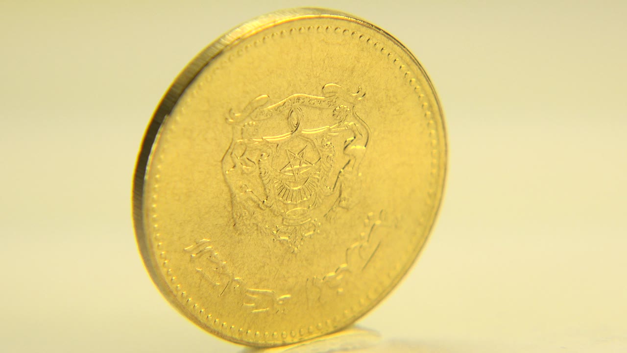 A gold doubloon-style coin stands nearly face-on under warm white light in Westminster, Colorado, with no visible people.