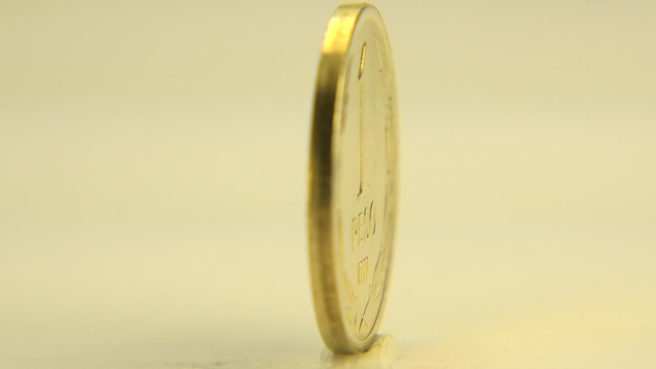 A gold-colored coin stands nearly edge-on on a pale revolving table in Westminster, Colorado, with warm yellow light and no visible people.
