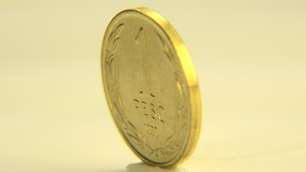 A gold-colored Republic of Chile coin stands upright on a pale surface in Westminster, Colorado, shown in soft warm focus with no visible people.