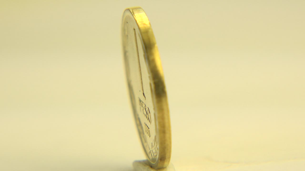 Thin edge view of a gold coin on a flat surface.