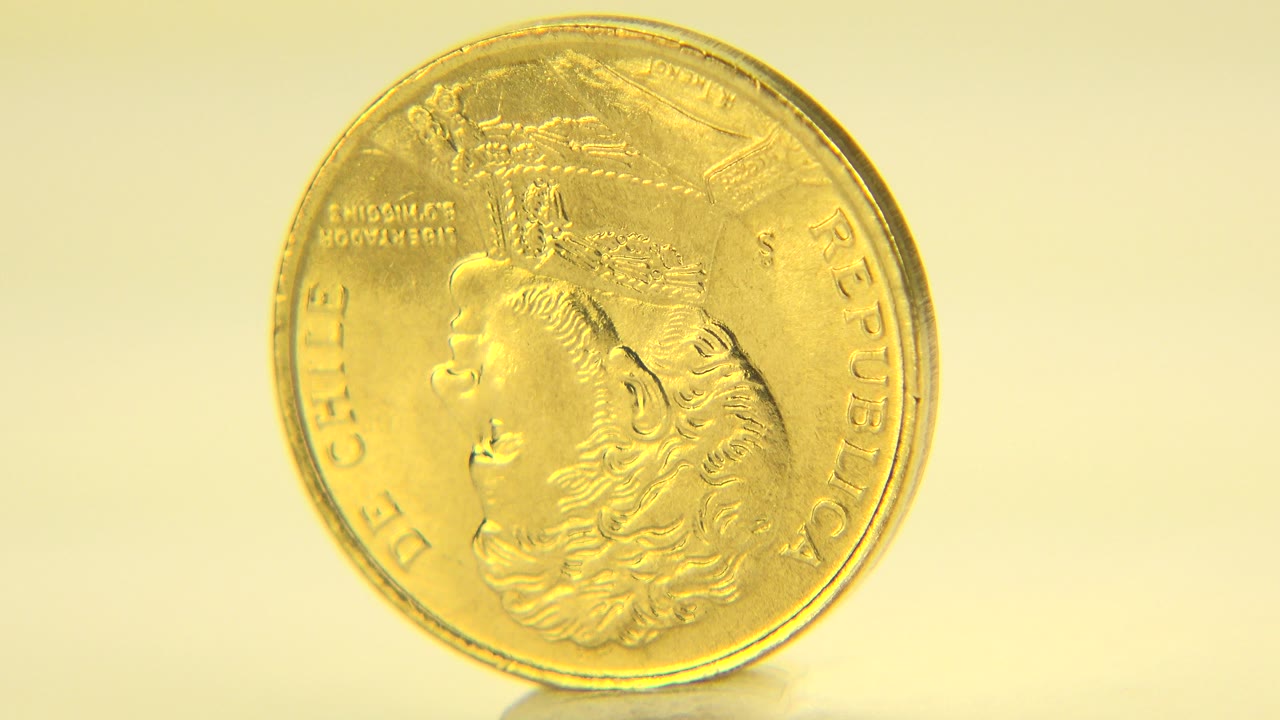 Gold-colored Chilean coin standing upright on a pale surface.