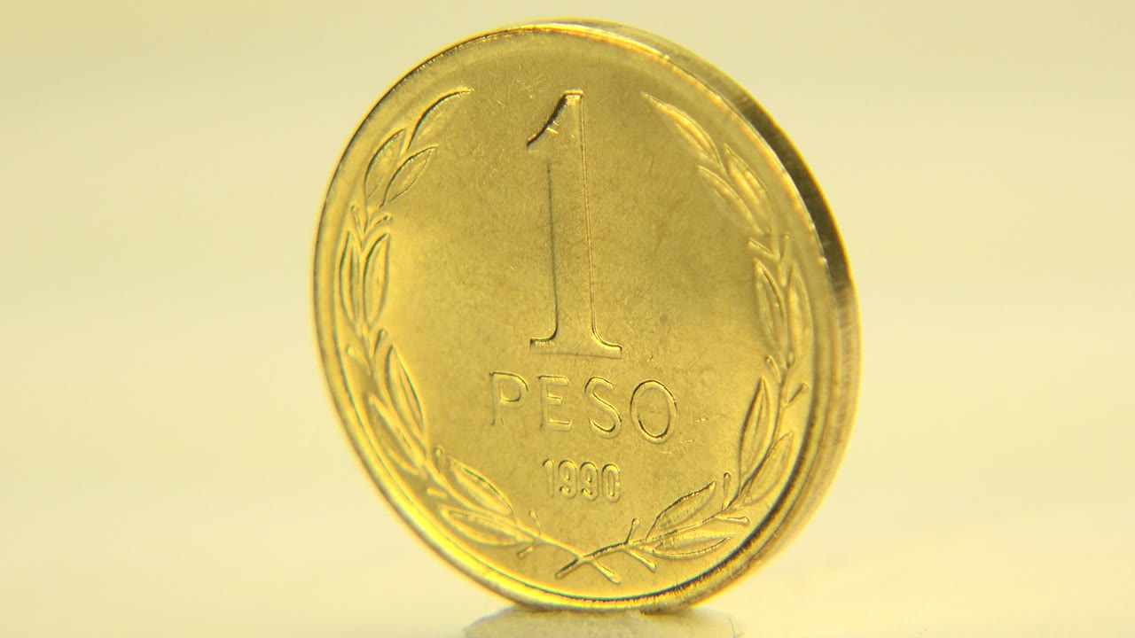 The Chilean one peso coin remains almost front-facing in Westminster, Colorado, with the embossed numeral, PESO text, and lower date visible, and no visible people.