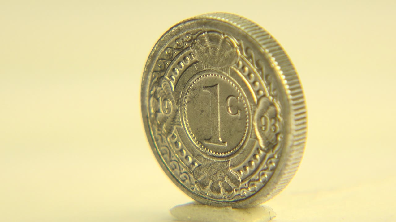 A thick metal coin stands nearly face-on while spinning on a pale tabletop in Westminster, Colorado, with warm yellow light and no visible people.