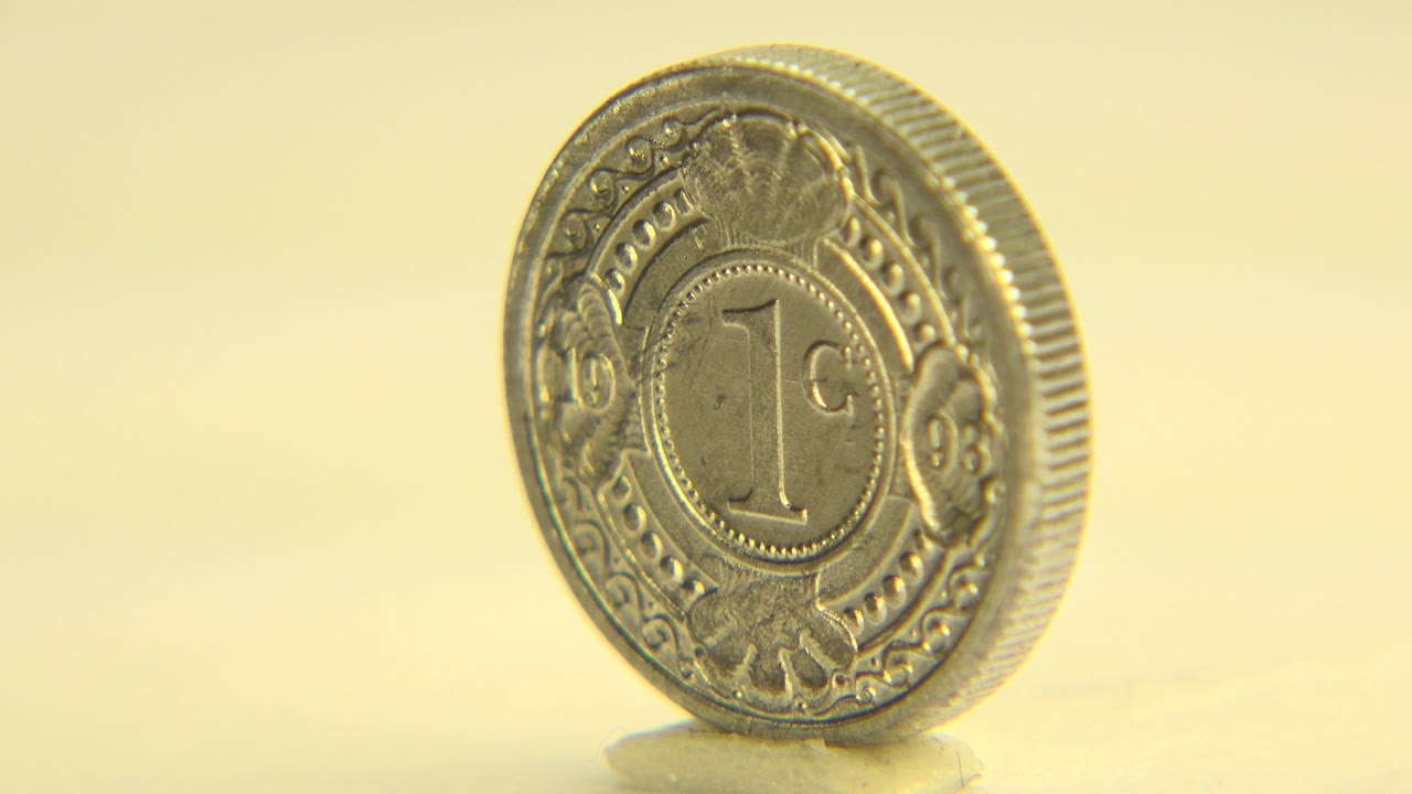The coin remains upright with its engraved front face visible, set against a soft yellow background in Westminster, Colorado, with no visible people.