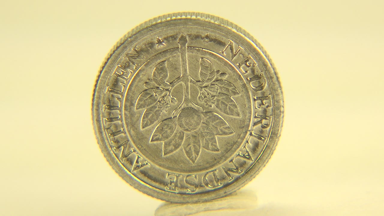 At 0:00, a coin stands nearly face-on on a pale tabletop in Westminster, Colorado, with warm yellow light and no visible people.