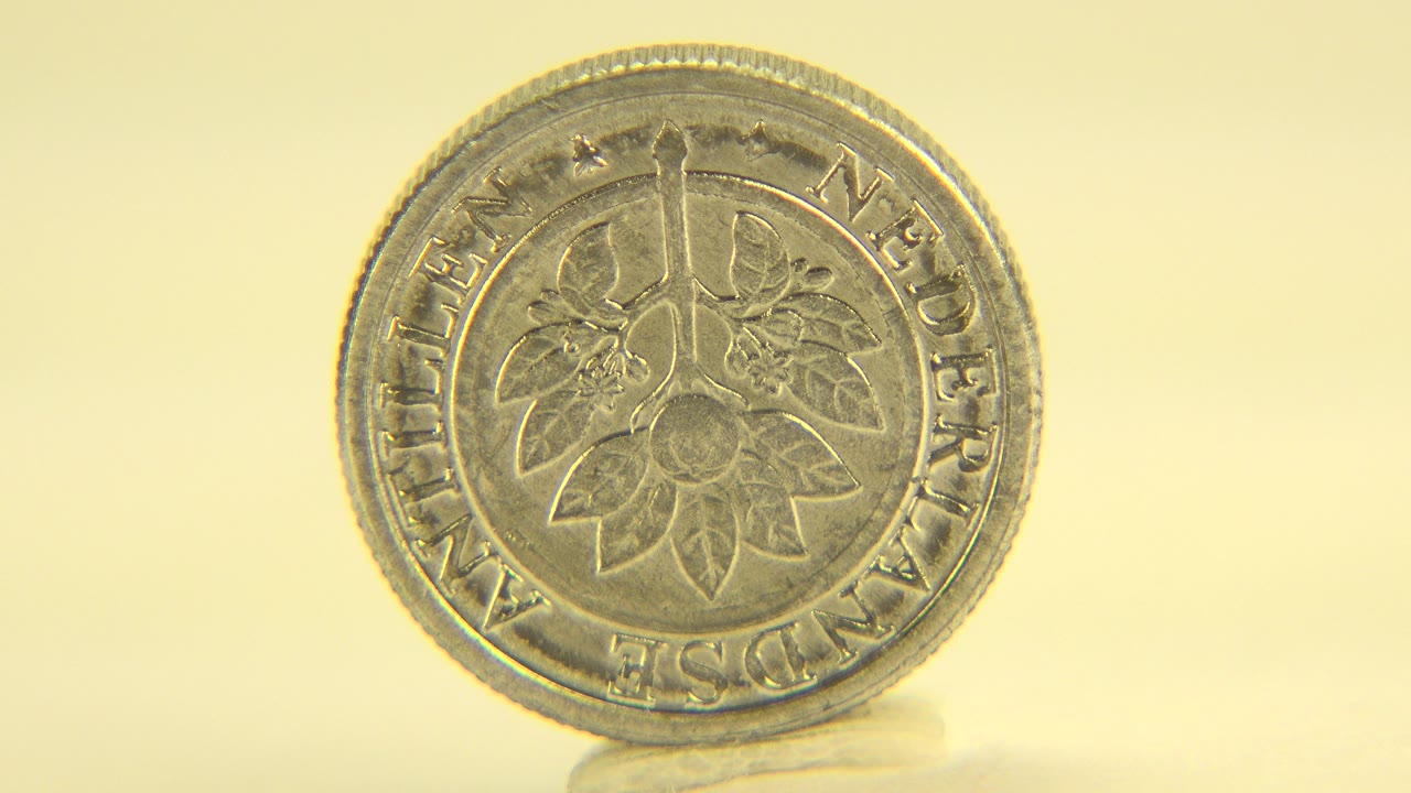 At 0:01, the coin is still mostly face-on and centered on the pale table, with shallow focus and no visible people.