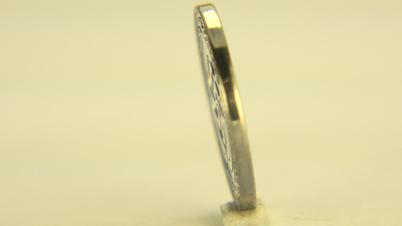 Thin edge of a standing coin on a yellow surface.