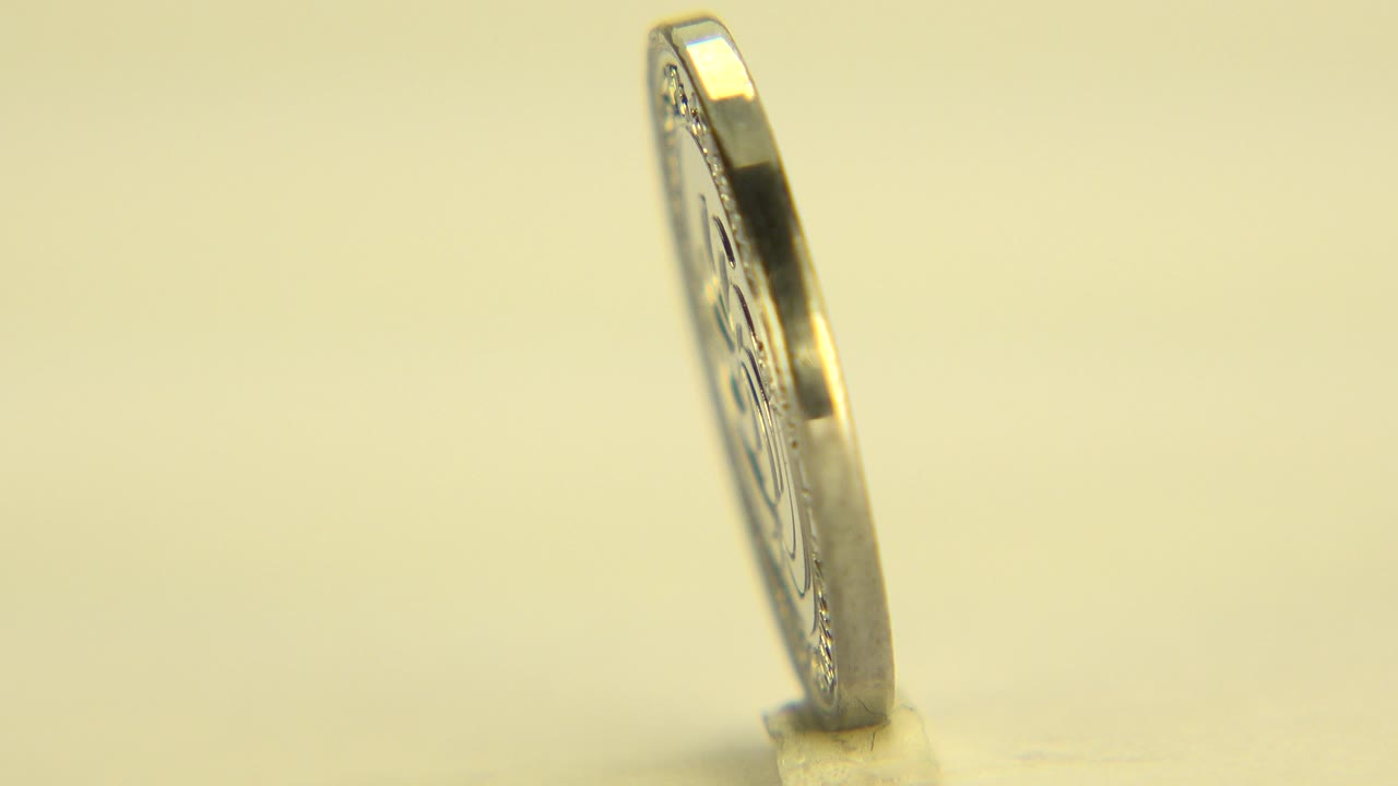 At the start of the Westminster, Colorado clip, the upright coin is mostly edge-on with a small base visible and no visible people.