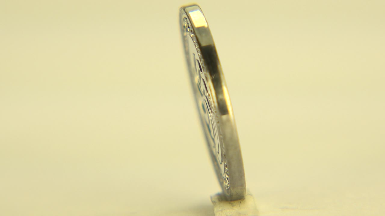 One second in, the coin remains in a slim edge view, catching bright highlights along its rim in the Westminster, Colorado home-movie frame, with no visible people.