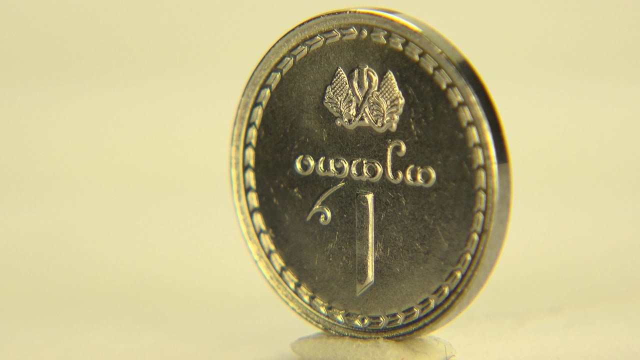 A silver coin stands nearly front-facing on a pale reflective surface in Westminster, Colorado, with a warm yellow background and no visible people.